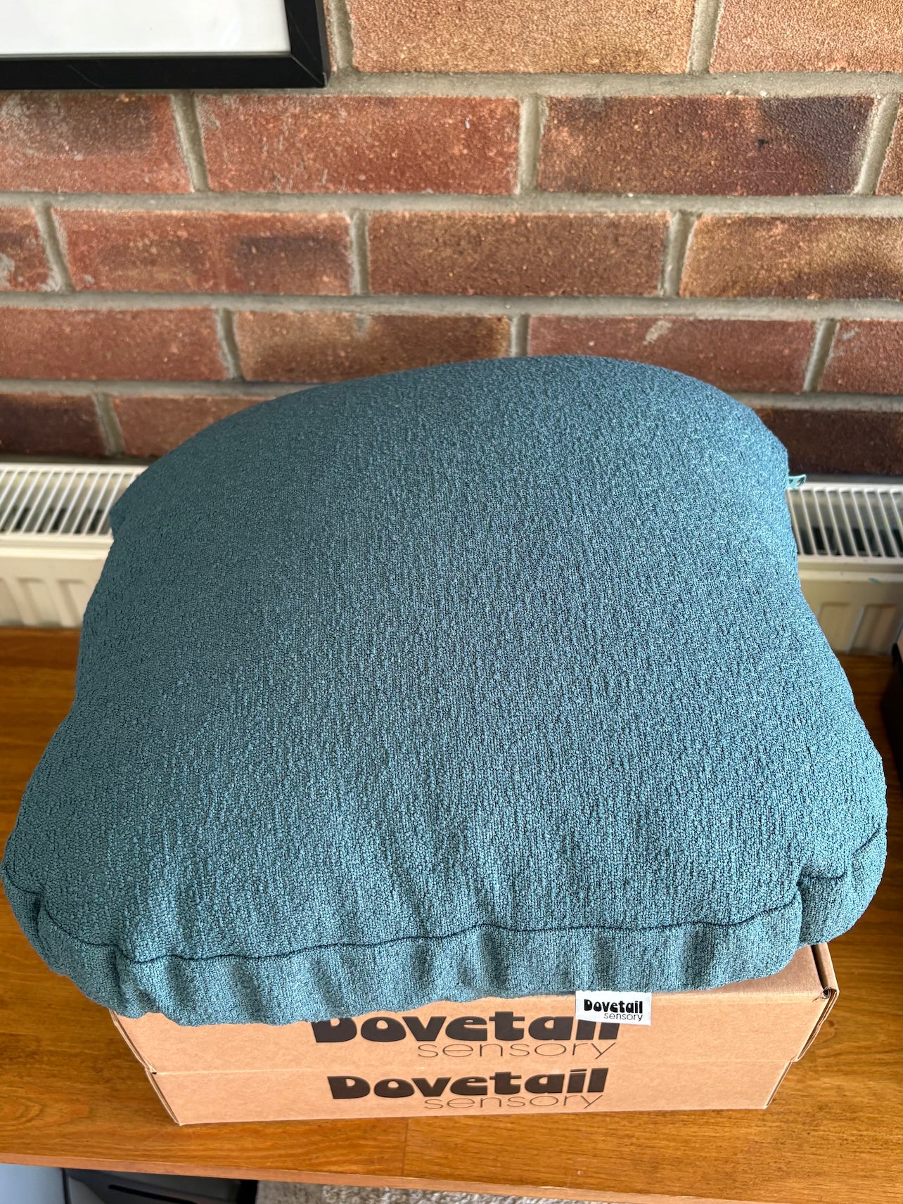 Blue cushion on a cardboard box with 'Dovetail sensory' branding against a brick wall.