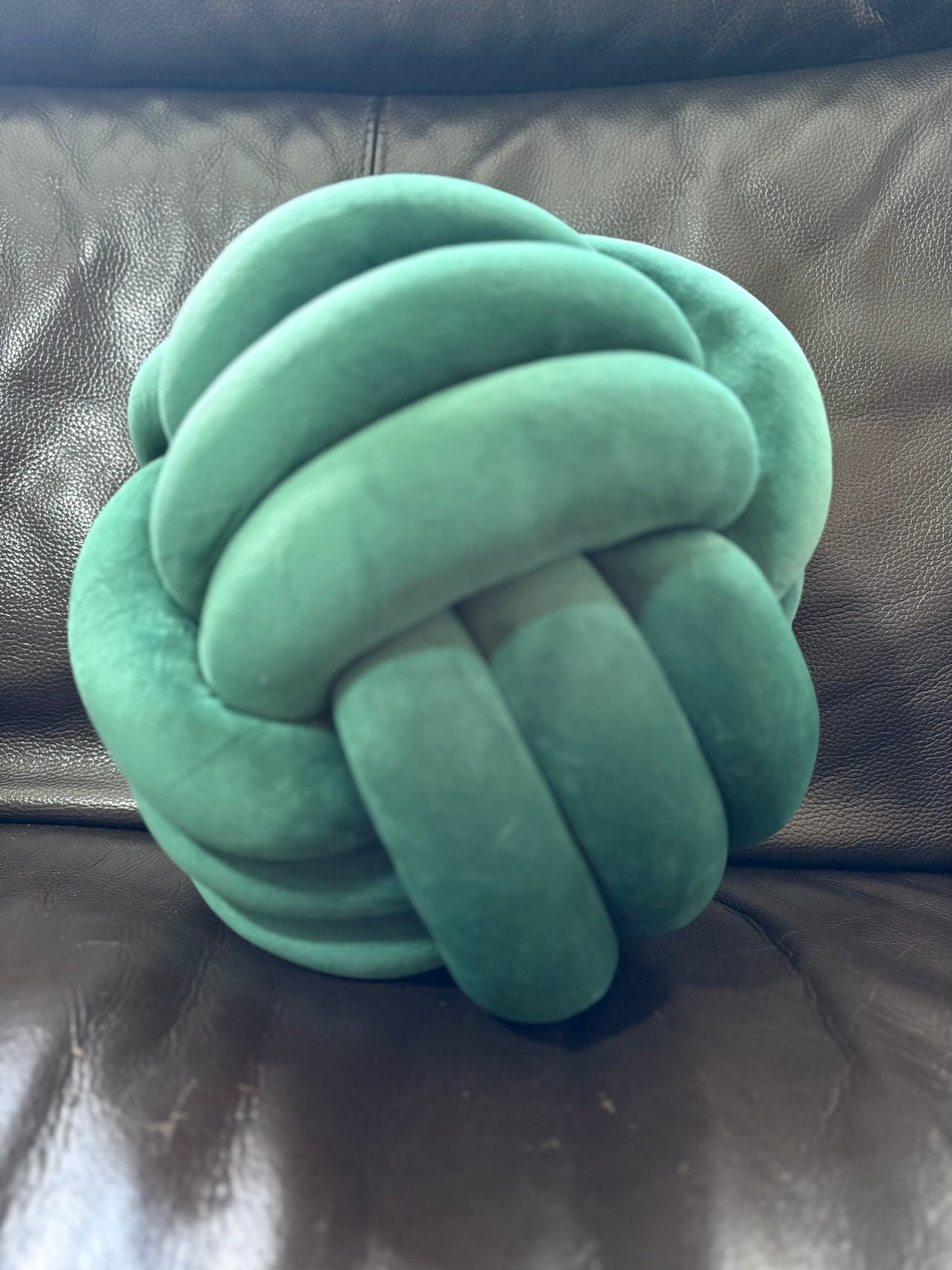 Green Dovetail sensory knotted pillow on a brown leather couch