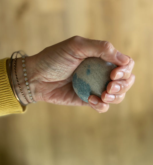 Hand holding a stone with a blue marking against a blurred natural background