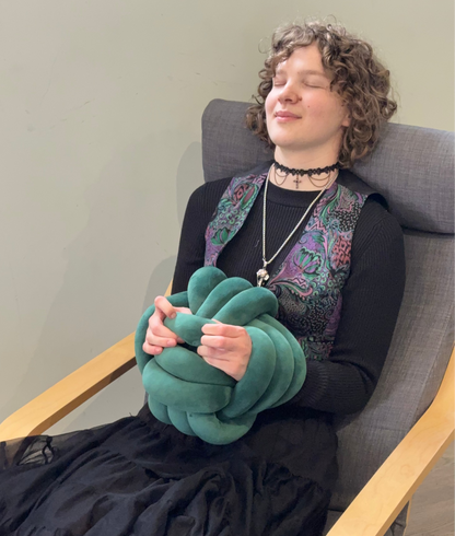Person sitting in a chair holding a green sensory knot ball, wearing a black dress.