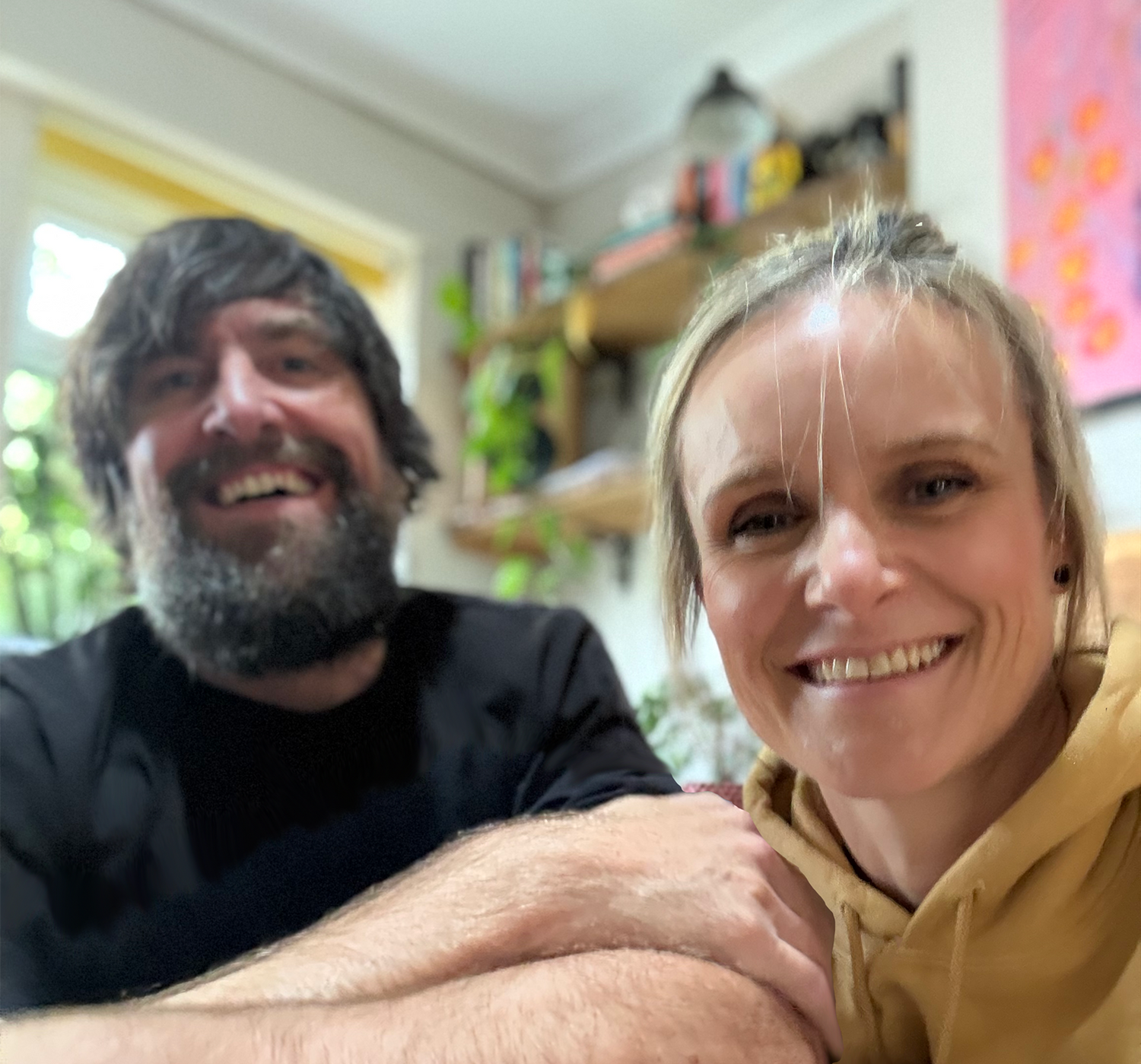 Two people sitting together in a room with shelves and plants in the background
