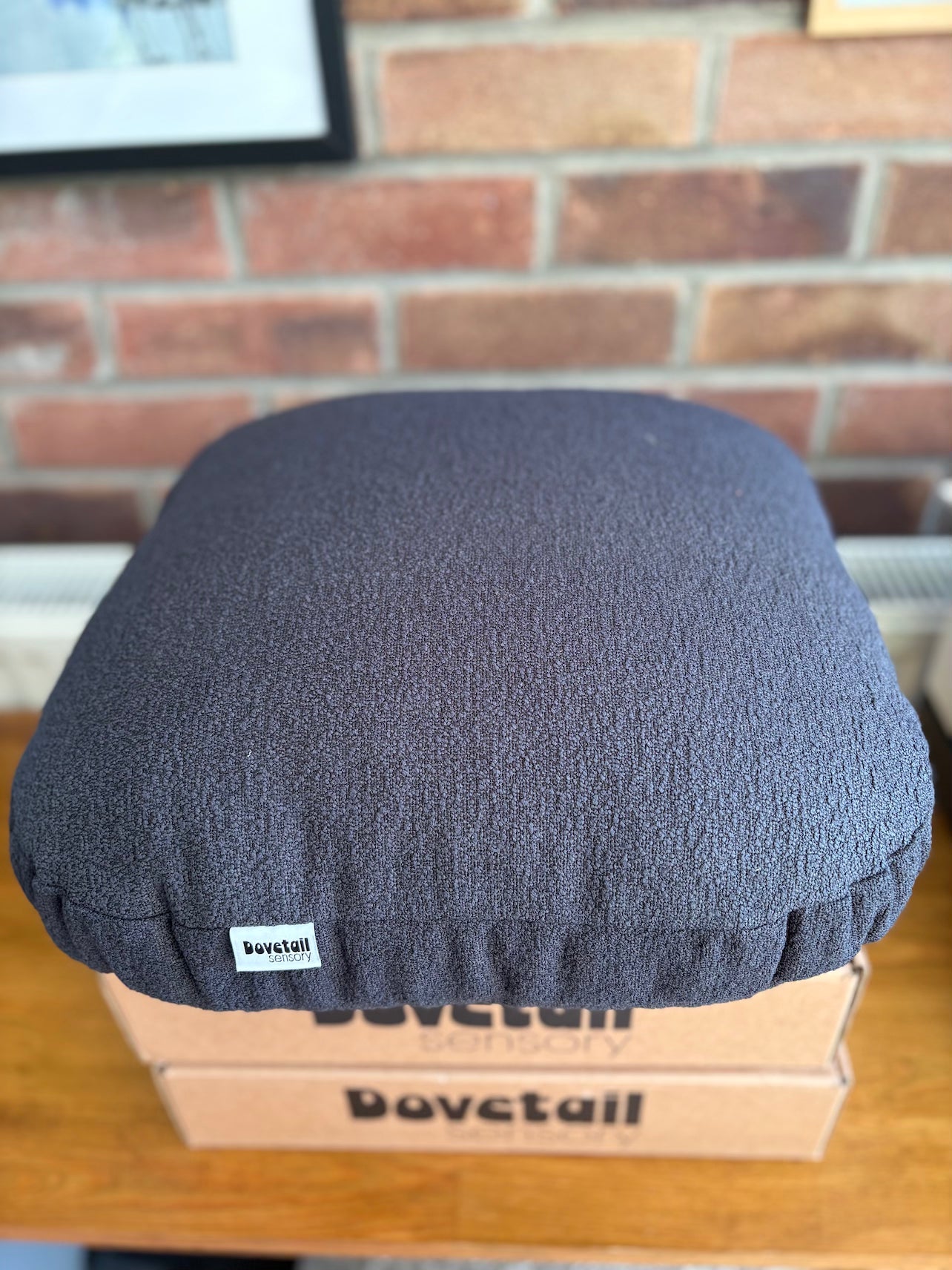 Grey cushion on a cardboard box with 'Dovetail sensory' branding against a brick wall.
