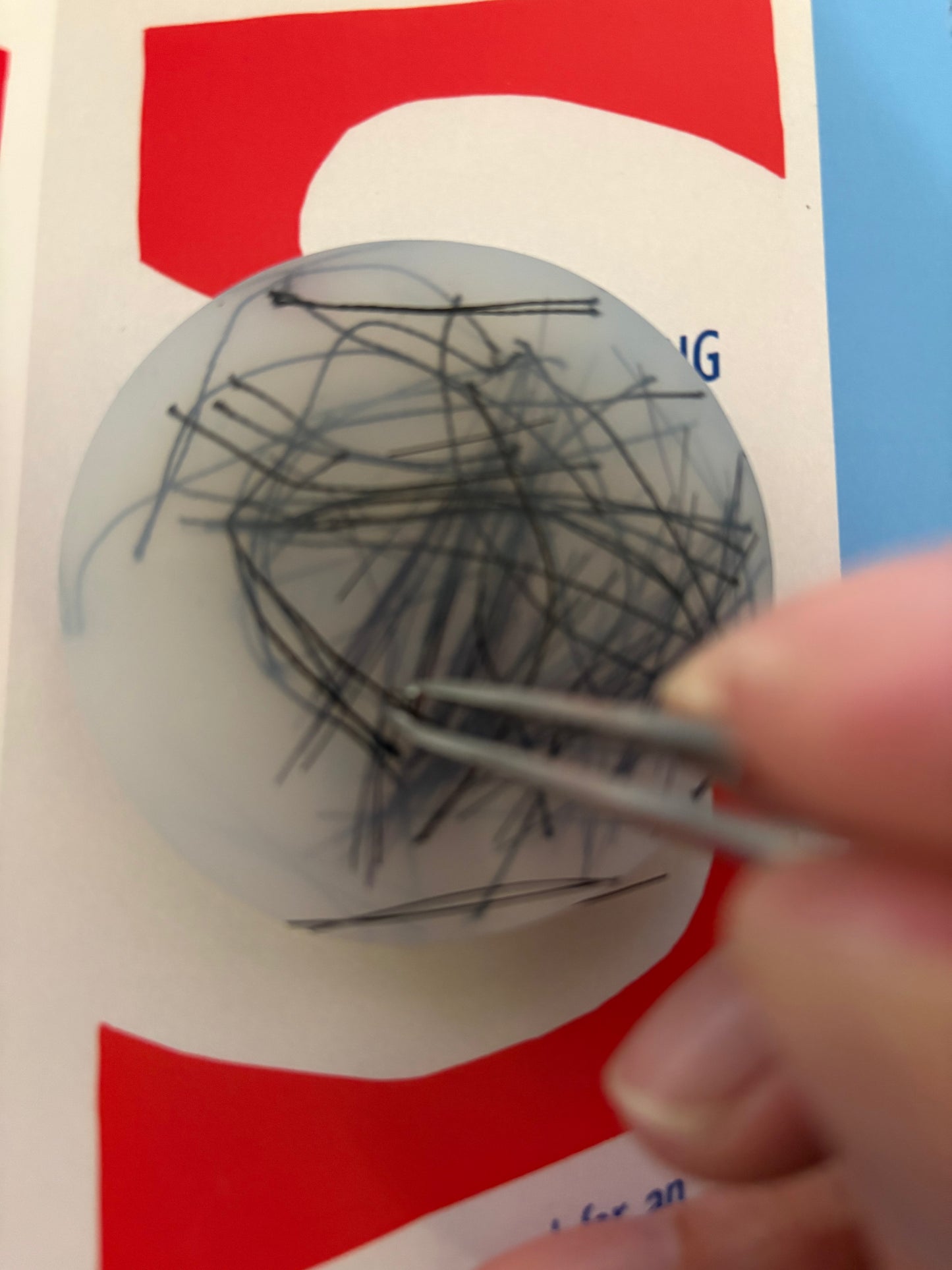 Close-up of a hand using tweezers to remove hairs from a ball with a red and white background