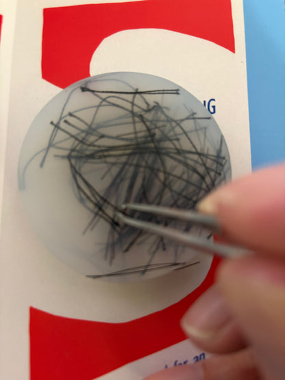 Close-up of a hand using tweezers to remove hairs from a ball with a red and white background