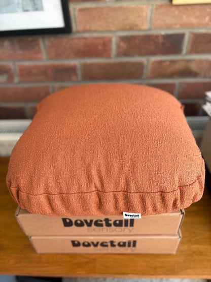 orange cushion on a cardboard box with 'Dovetail sensory' branding against a brick wall.
