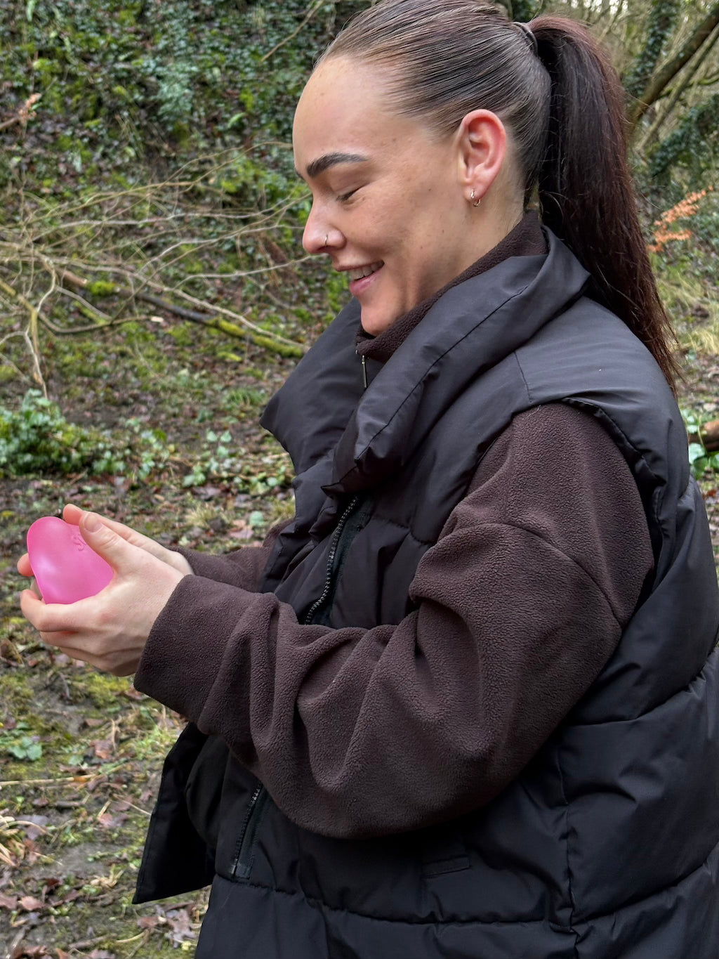 Person holding a pink object outdoors with trees and foliage in the background