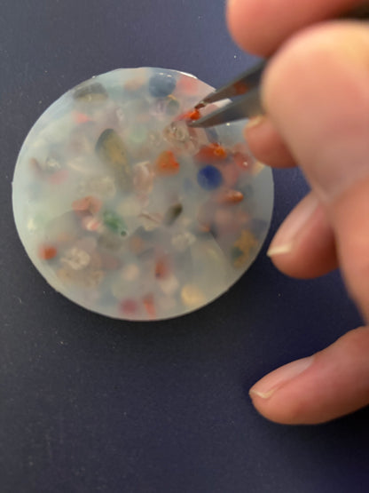 Round resin object with colorful beads being held by a hand against a blue background